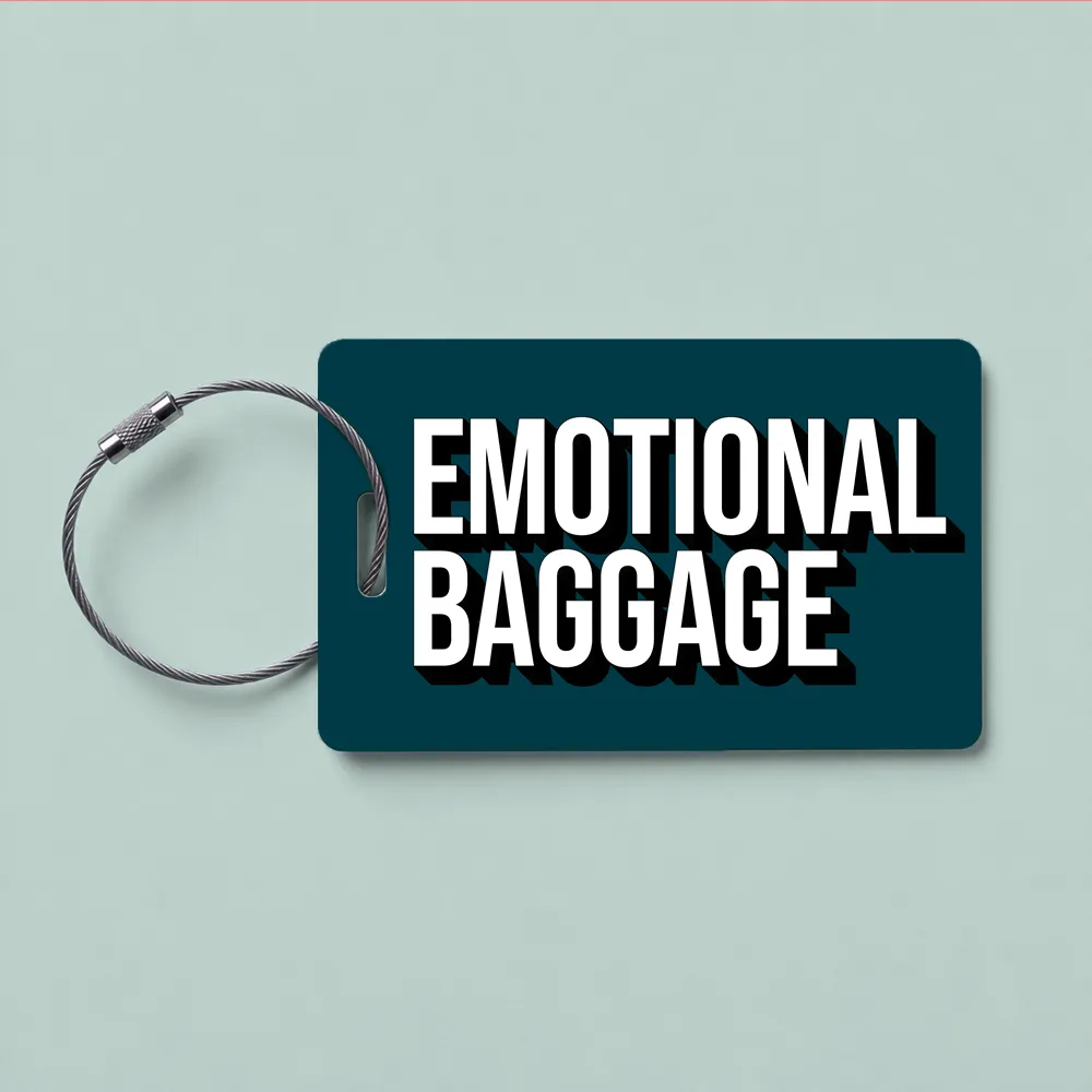Teal luggage tag with the bold text 'EMOTIONAL BAGGAGE' and a metal loop on a pale blue background.
