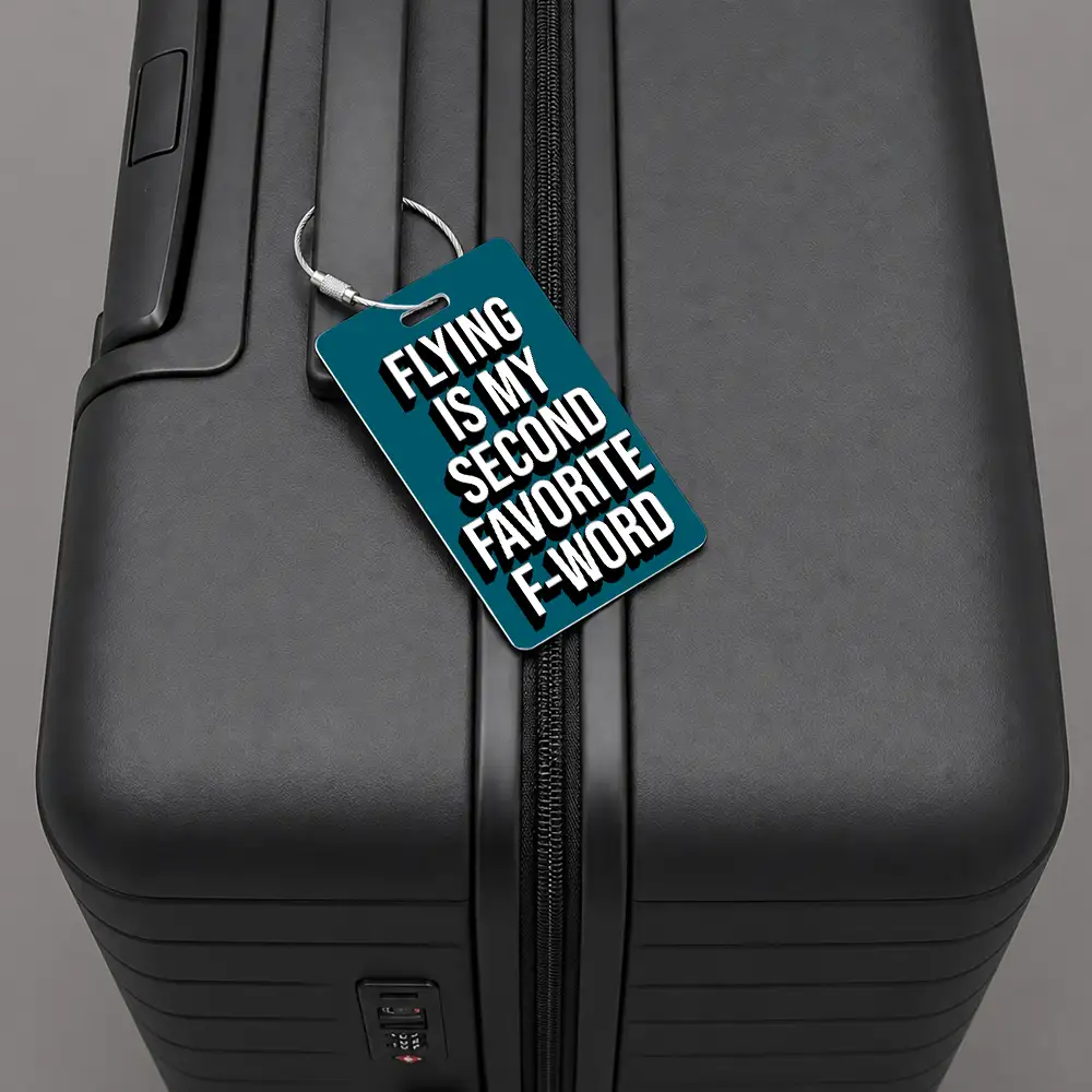 Close-up of a black hard-shell suitcase with a teal luggage tag that reads, 'Flying is my second favorite F-word'.