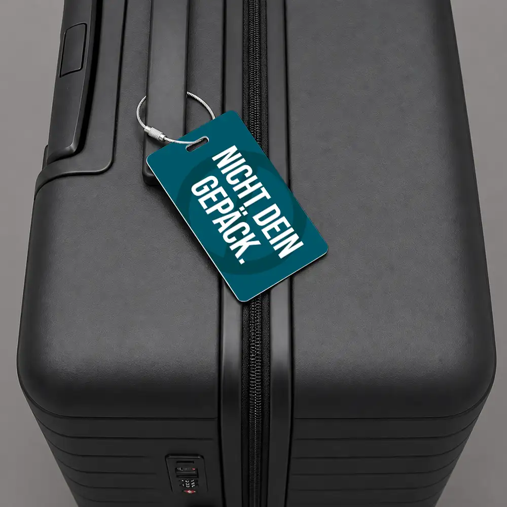Close-up of a black hard-shell suitcase with a teal luggage tag attached to the zipper pull.