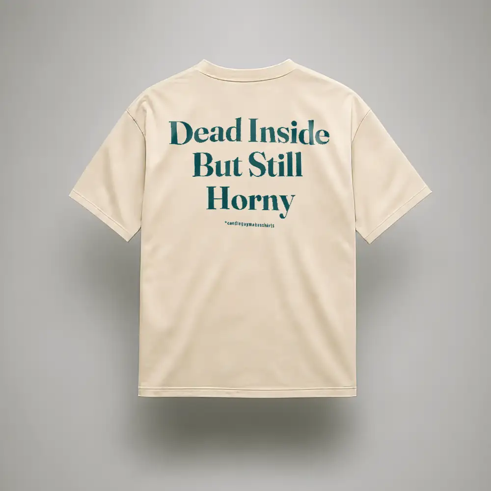 Beige T-shirt laid flat with teal slogan: 'Dead Inside But Still Horny' on the back surface.