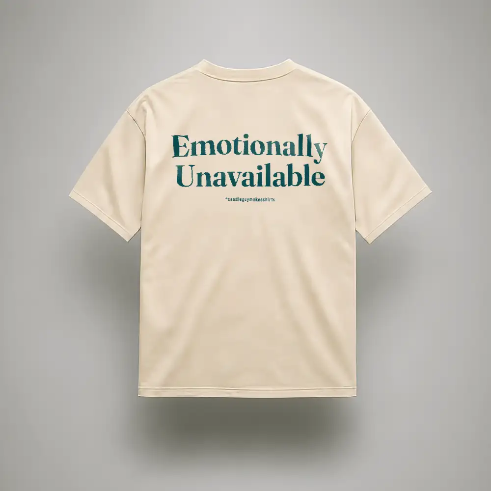 Beige T-shirt shown from the back with teal text reading 'Emotionally Unavailable' and small hashtag under it.