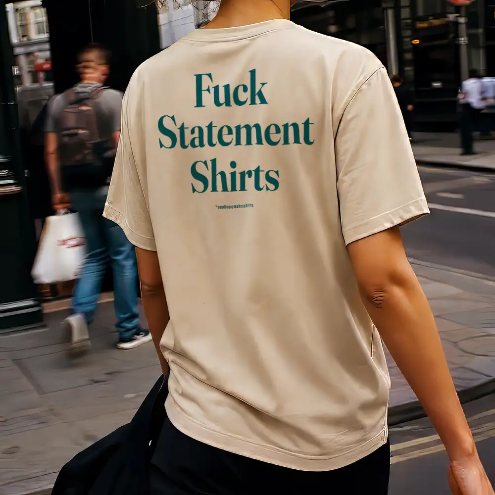 Person walking away wearing a beige T-shirt with teal text on the back that reads 'Fuck Statement Shirts'.
